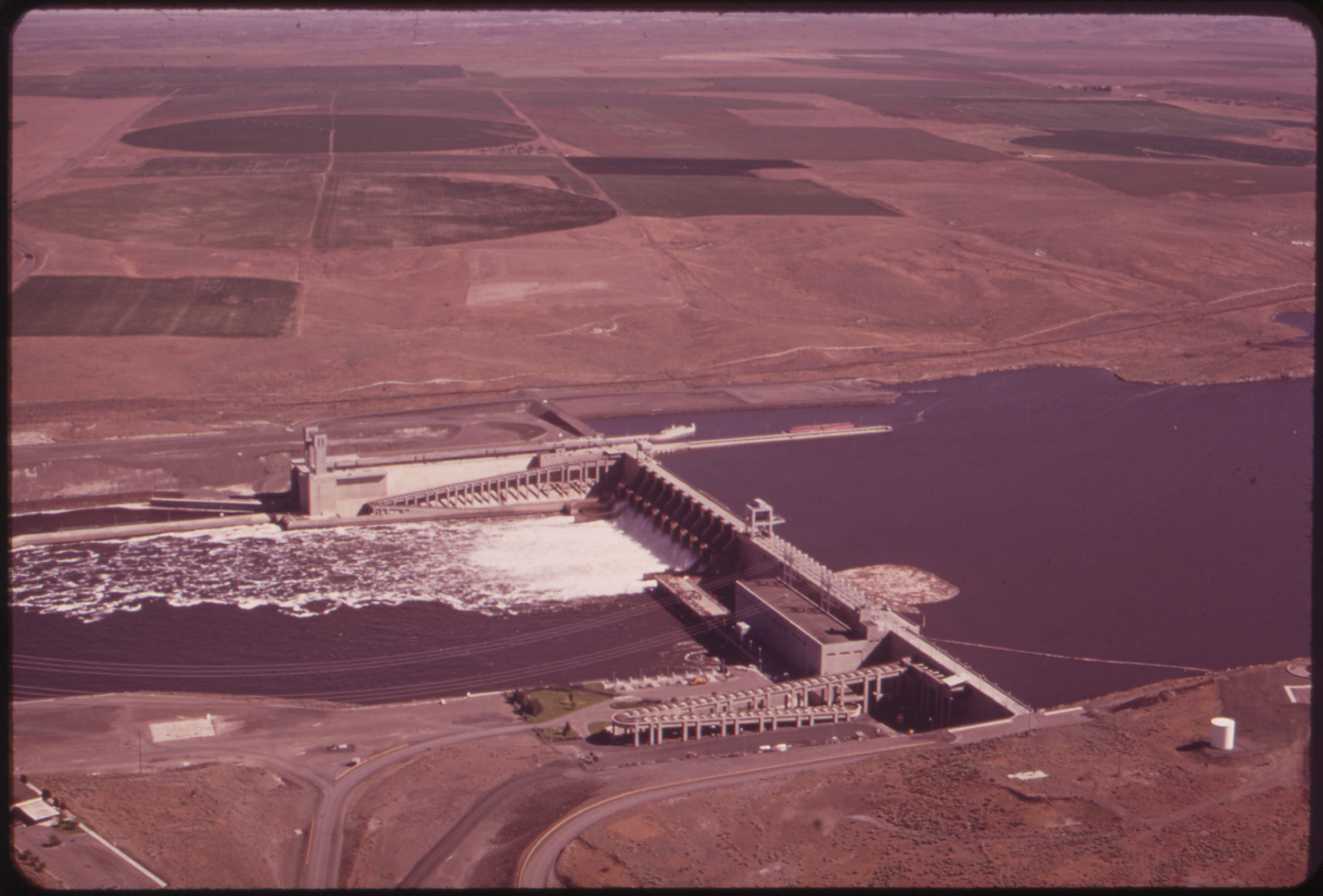 Aerial photograph of Ice Harbor Dam on the Snake River, water spilling over the gates, surrounded by dry farmland.